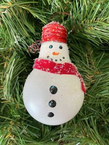 Light bulb snowman hangs in green Christmas tree 